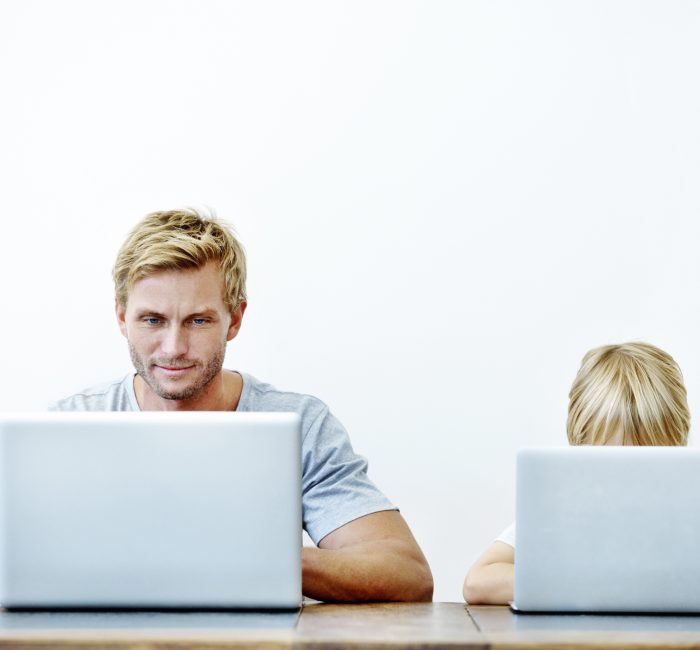 A young father and his son sitting together on their laptops